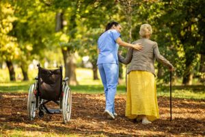 A caregiver assisting an older adult with medication at a small dining table in a bright, homey setting.