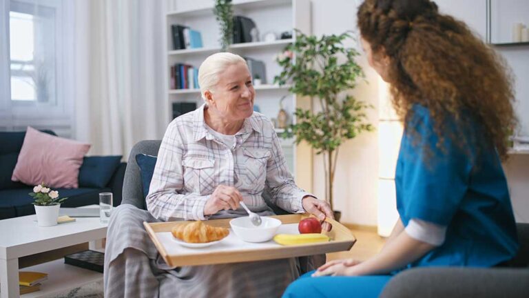 An older adult and family member packing boxes together in a cozy, furnished living room.