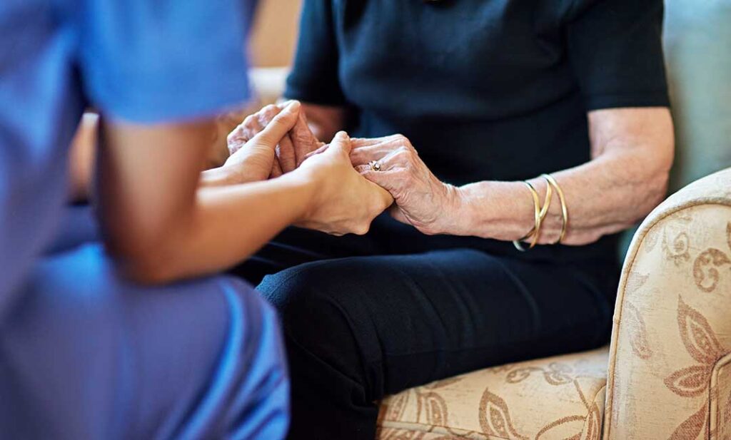 An older adult and family member pack personal items into boxes together in a cozy living room.
