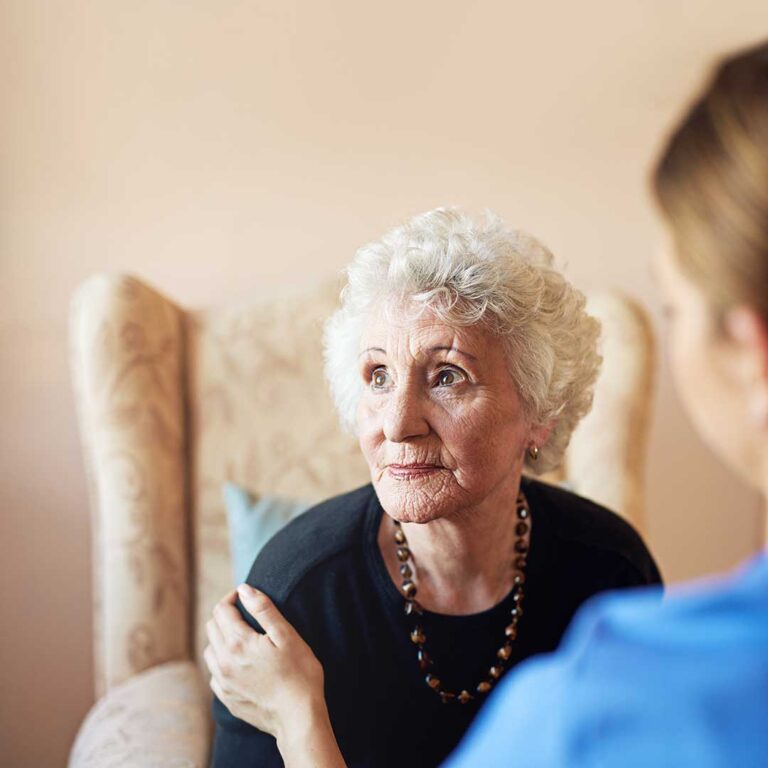 Older resident arranging family photos and a quilt in a bright assisted living apartment.